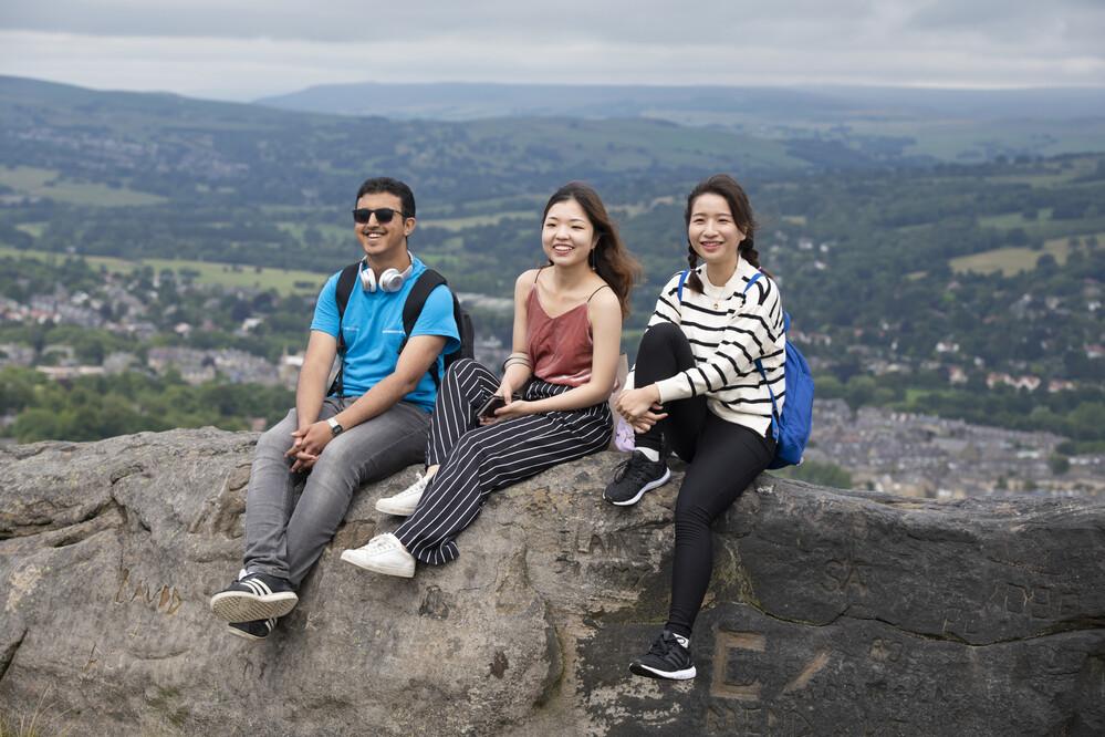 A group of students are sitting on some rocks with a view of countryside behind them