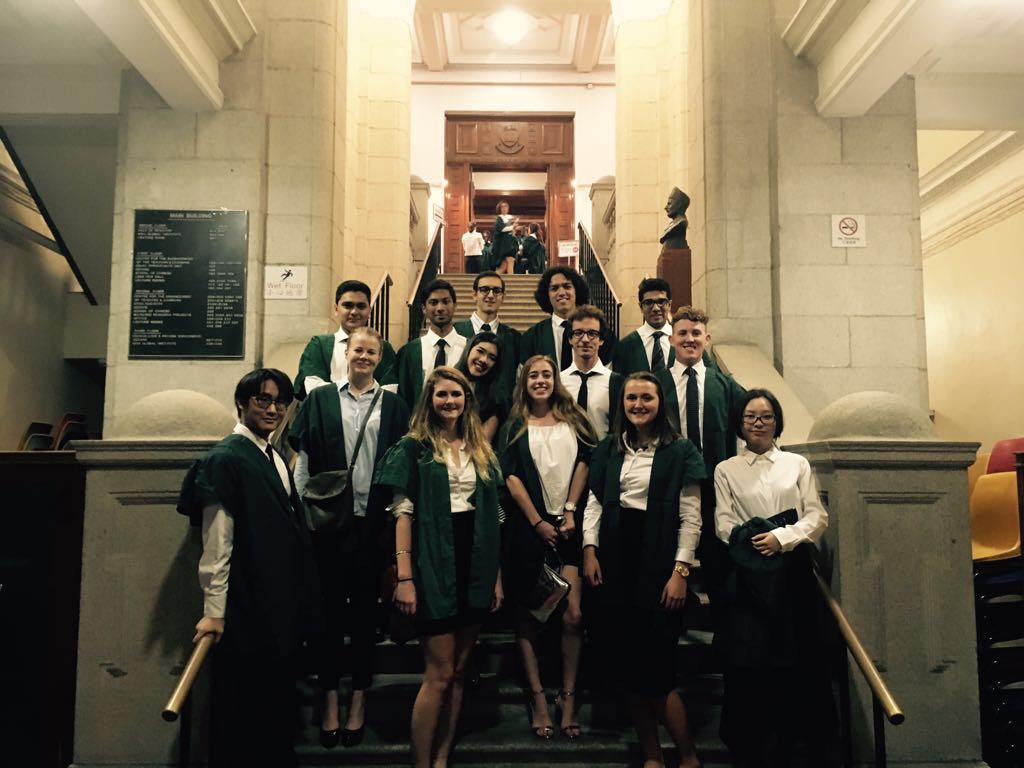 Students wearing green gowns stand for a photo on steps