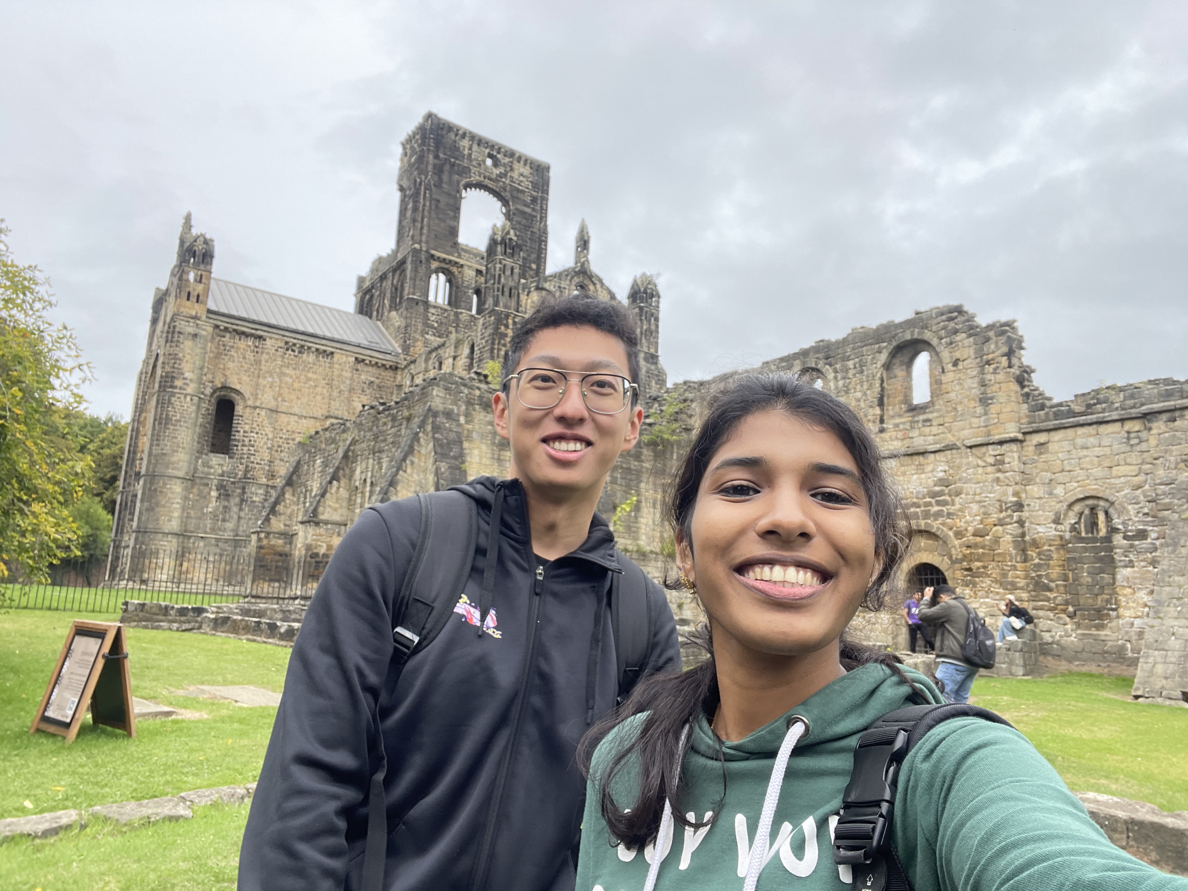Two students standing in front of Kirkstall Abbey smiling.