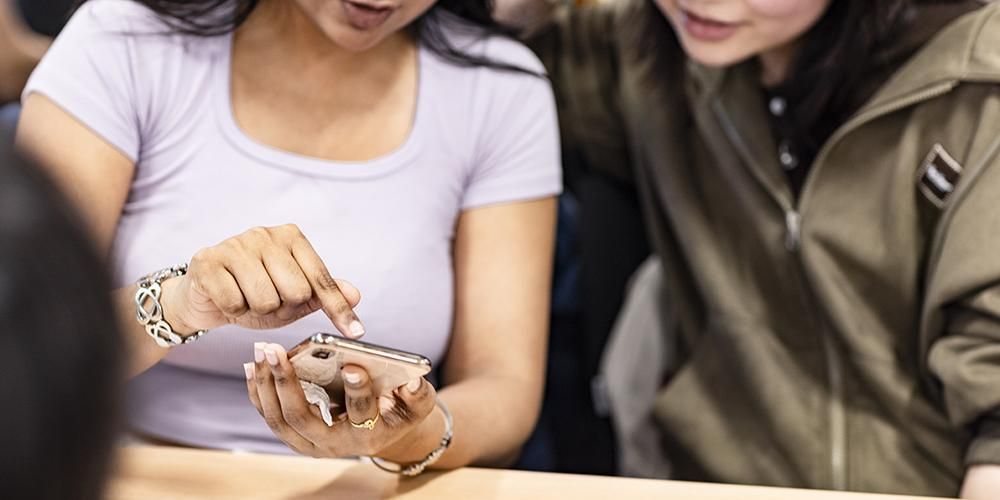 Two students looking at a phone screen, one is pointing to the phone