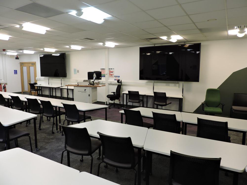 A large room with tables and chairs and a large screen