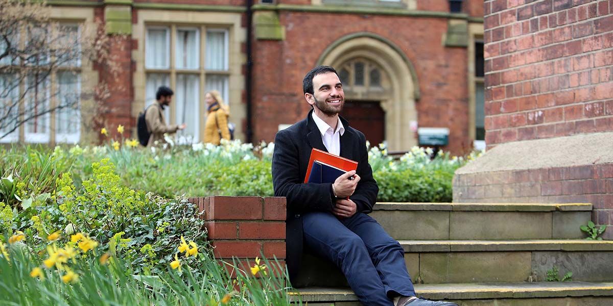 Postgraduate research student sits on the steps next to The Great Hall in Clothworkers' Court and smiles