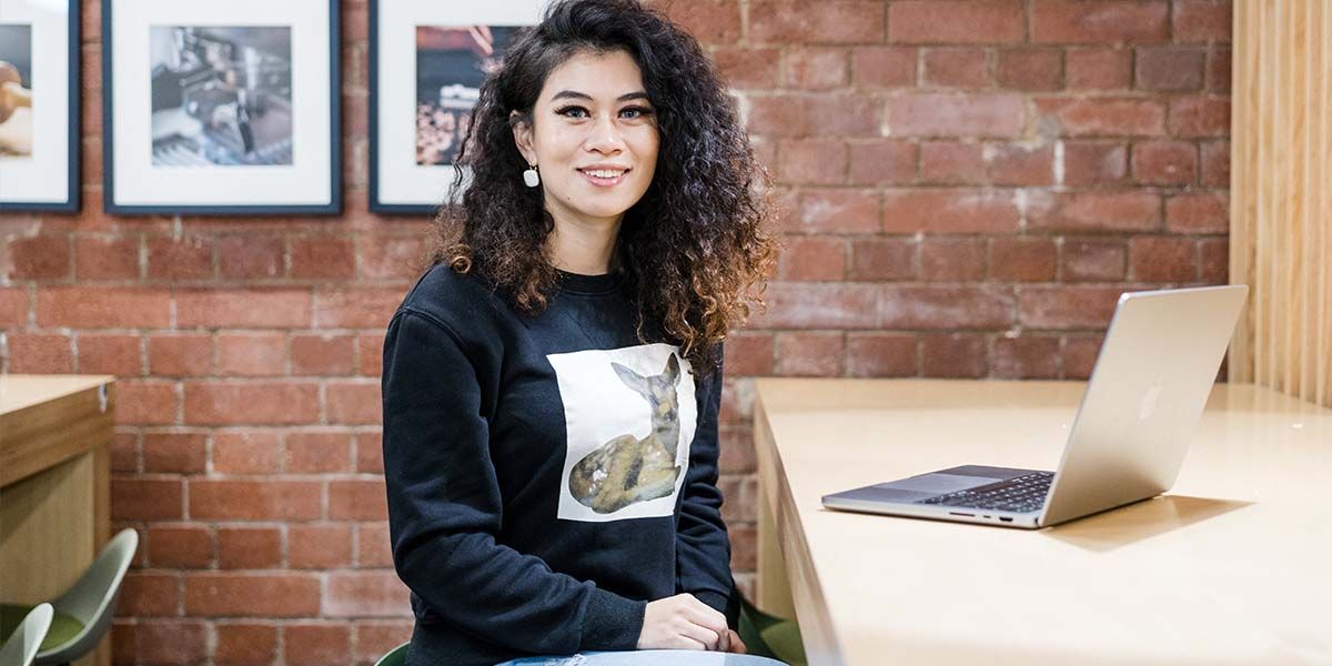 A student sits at a table and looks to camera inside a cafe on campus.