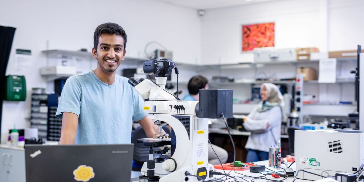 Postgraduate research student, Devesh Mistry, stands behind a bench containing equipment inside a laboratory and looks towards the camera.