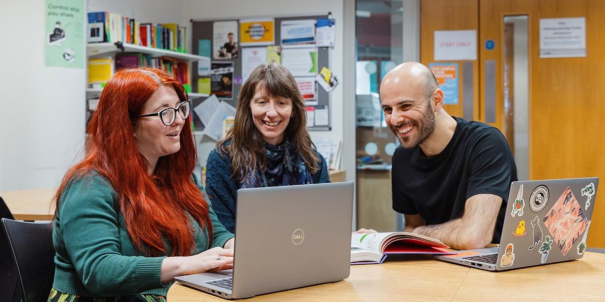 Three Foundation Year students working together on a laptop and smiling
