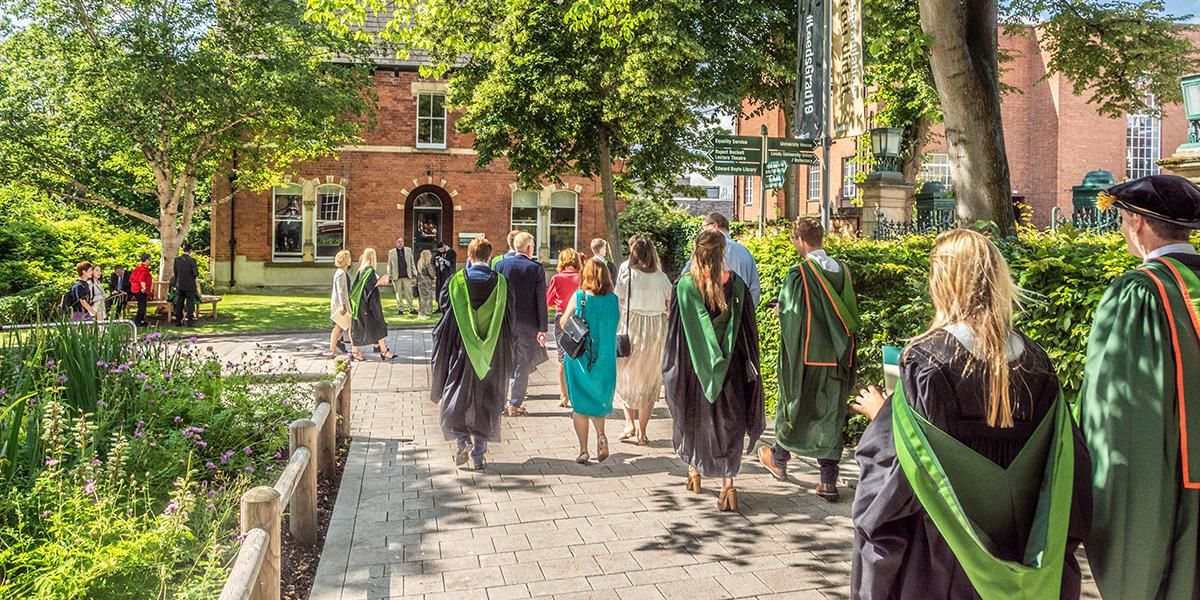 Graduates in gowns walking with their guests on campus in summer