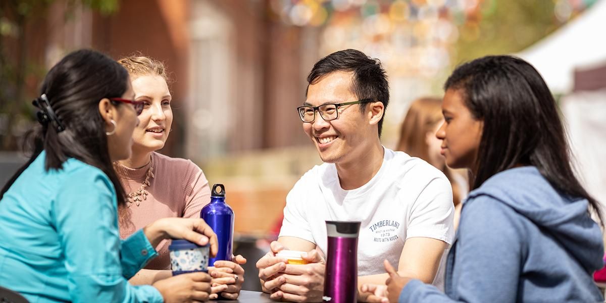 Four international students chatting to each other drinking hot drinks outside Leeds University Union