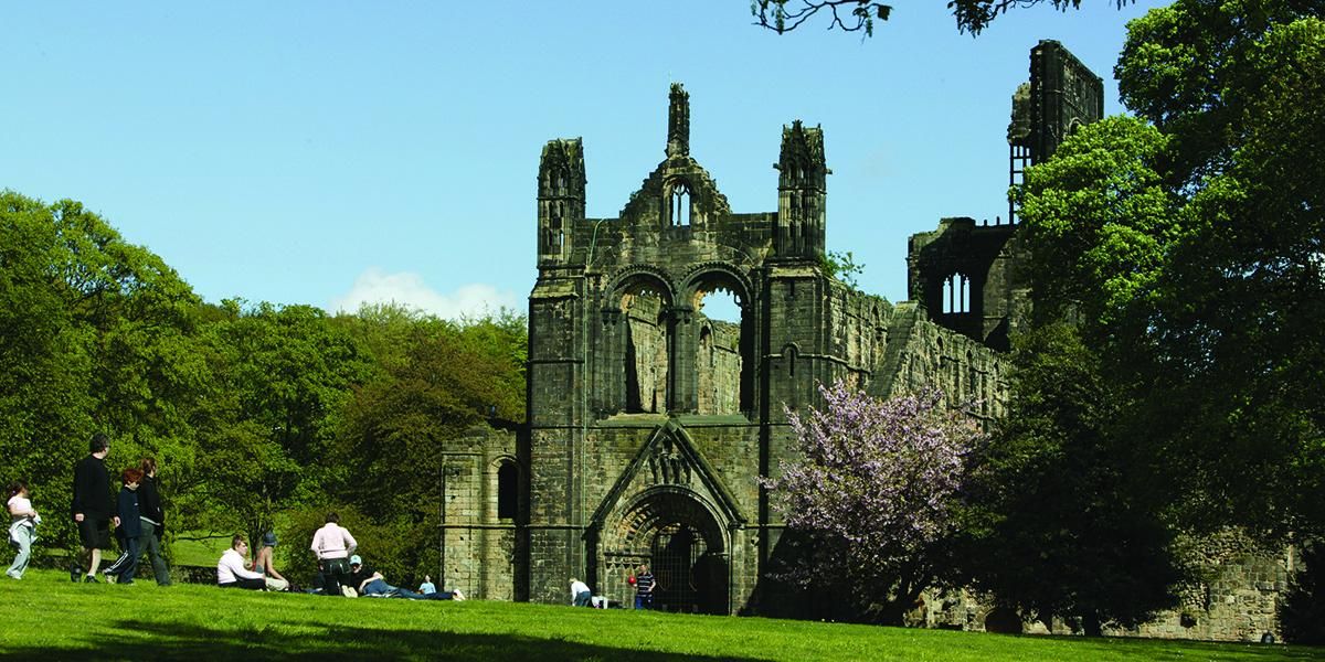 Kirkstall Abbey in summer with people sitting on the grass