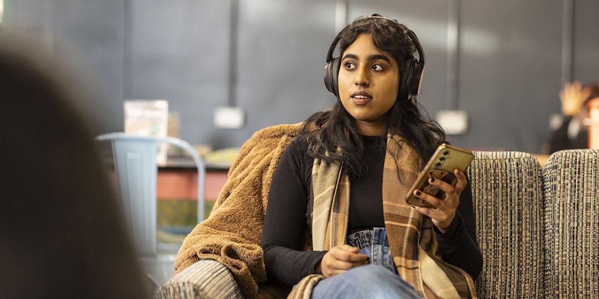 Student sitting on a sofa in a cafe holding a phone
