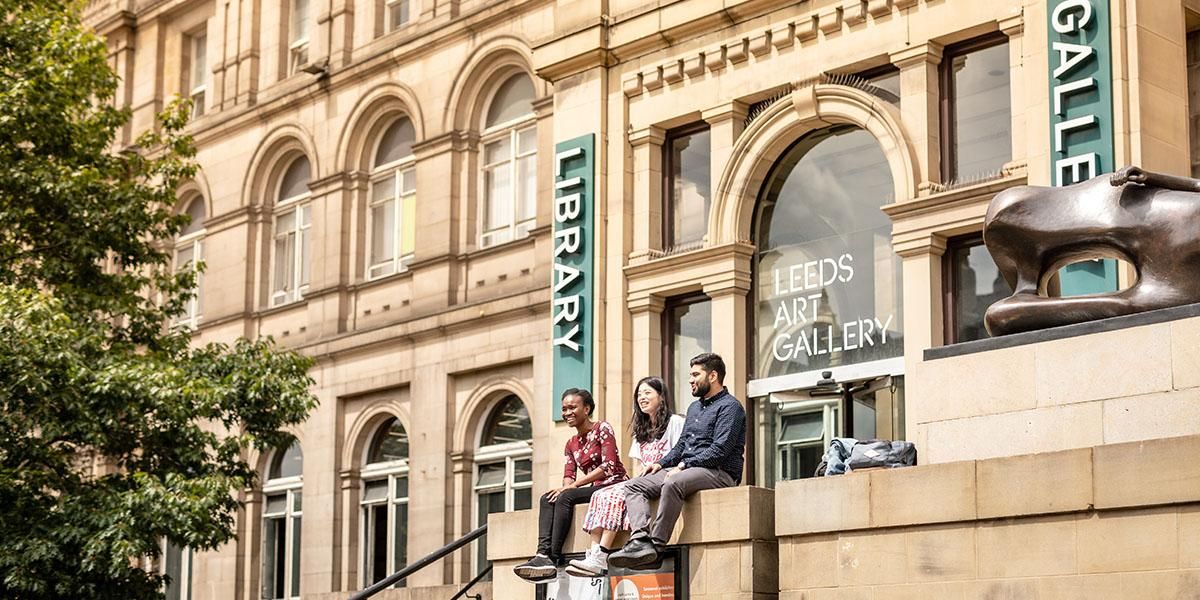 Three students sitting on a wall outside the entrance to Leeds Art Gallery