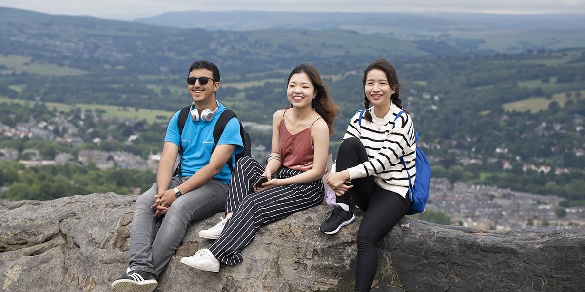 Three students sitting on a rock on Ilkley Moor surrounded by countryside