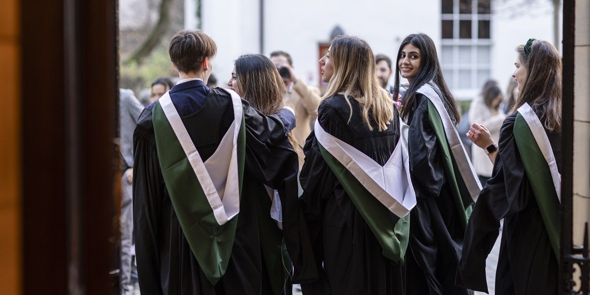 A group of students on graduation day in their graduation gowns. One is turning round and smiling.