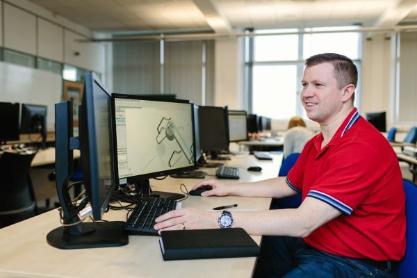 A mature students sits at a computer, working with multiple monitor screens.