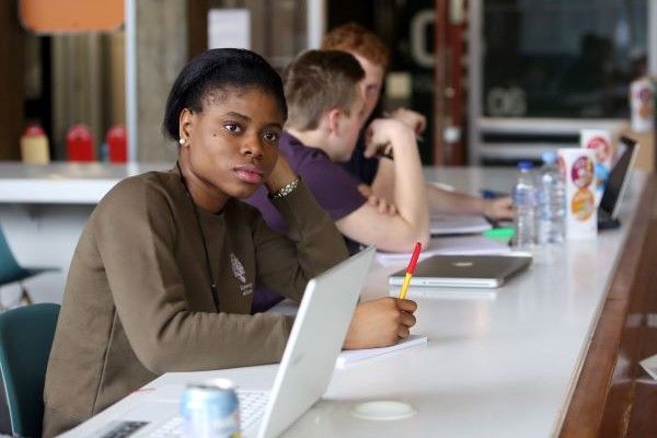 A student is in a classroom, with a pen in her hand, looking forward.