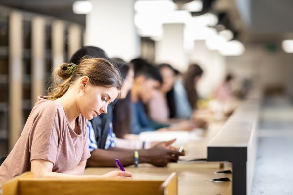 A row of students writing, with the camera focused on one student specifically.