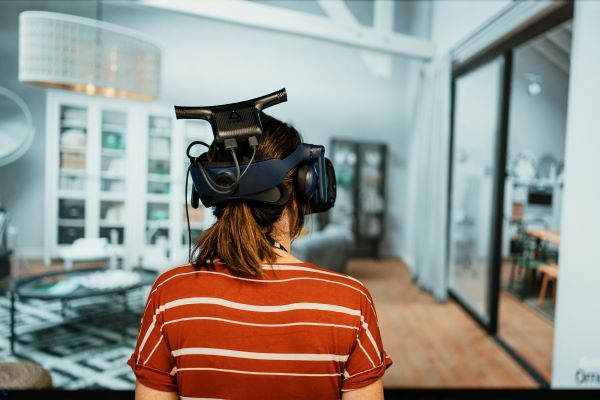 A person stands, turned away from the camera. They have a VR headset on, shown by the straps round their head.