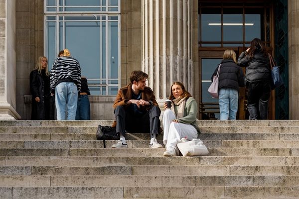 Two students sat on the Parkinson Building steps chatting with some students in the background.