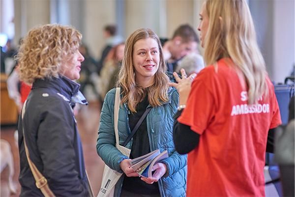 At the February 2020 Postgraduate Open Day at the University of Leeds, the Parkinson Court Fair showcases prospective students, families, and staff in red t-shirts interacting amid the iconic pillars of the Parkinson building.