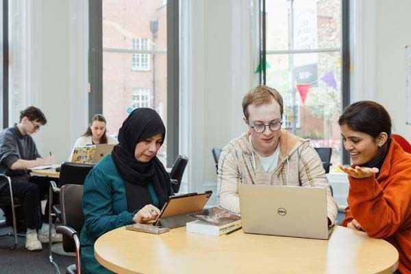 A group of mature students sitting at a table working n laptops and tablets