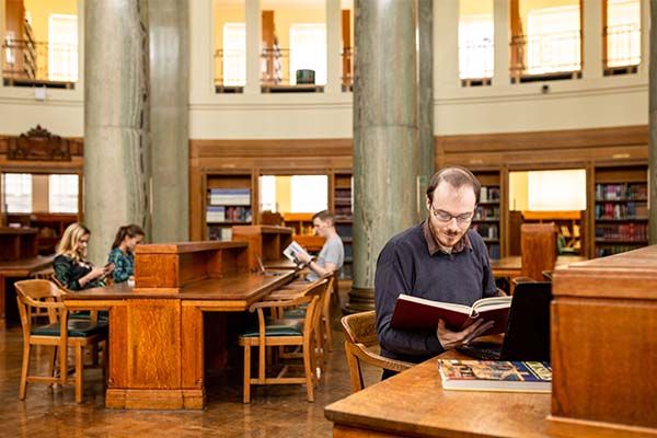 Postgraduate research student, sits at a desk in the Brotherton Library and reads a large book.