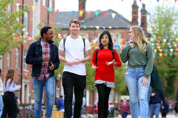 A group of four postgraduates walking outside on campus, past the Student Union, chatting and smiling.