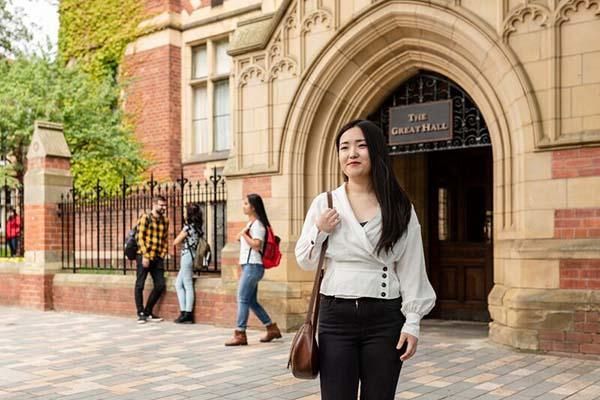 A smiling student stands on a pedestrianised area in front of The Great Hall on campus, in summer.