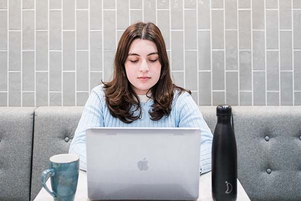 Student in a cafe working on a laptop facing the camera.