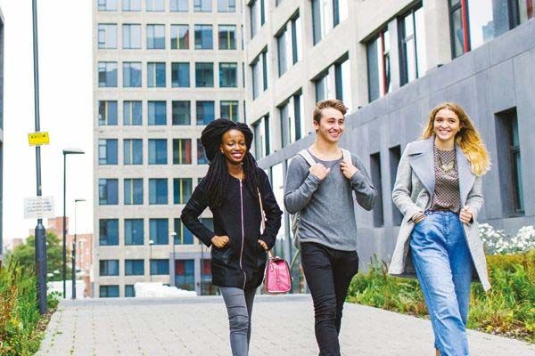 Three students chatting as they walk down a wide path next to a modern building.