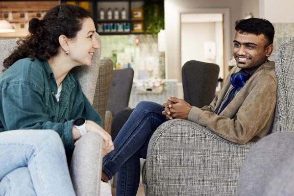 Two students sat in a cafe on sofas, chatting and smiling.