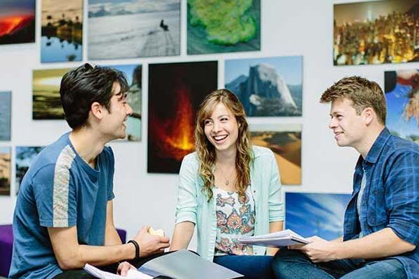 Students chatting and laughing together in a communal room on campus with posters on the wall behind them.