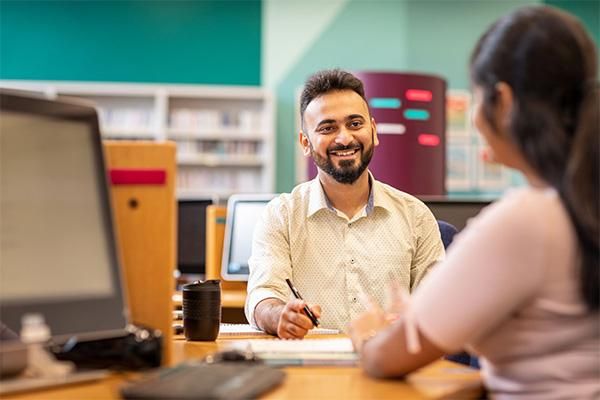 Student smiling and talking with an academic personal tutor at a desk in a study space.