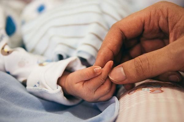 A baby's hand holding a parent's hand