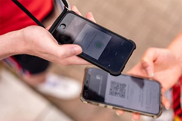 Close-up of two students holding smartphones, one showing a QR code and the other displaying a digital check-in screen