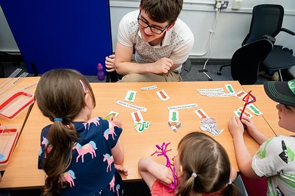 Three children supervised by an adult doing an activity with paper and pipe cleaners at Be Curious