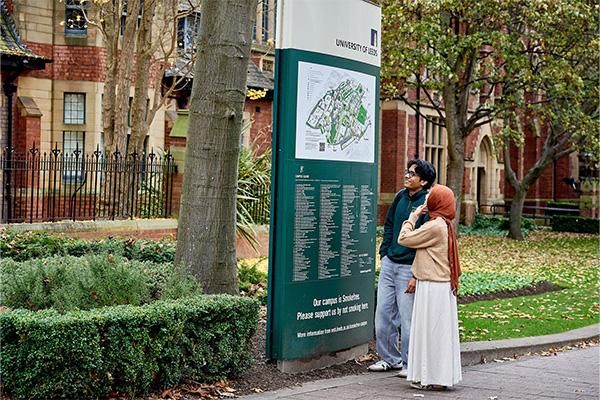 Two students standing outside looking at a large University of Leeds campus map and directory sign.