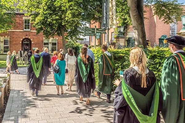 Graduates in gowns walking with their guests on campus in summer