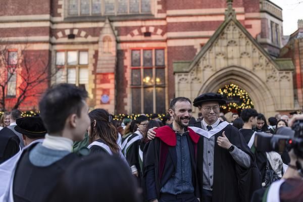 Two graduates having their photo taken outside the Great Hall that is lit up on graduation day