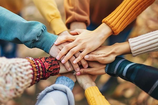 A group of people putting their hands on top of other hands  in a circle