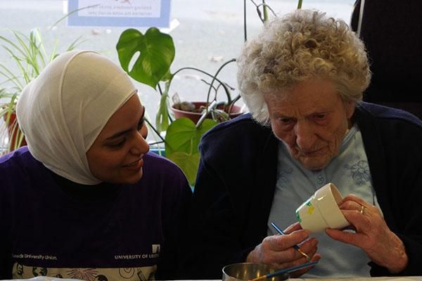 An intercultural ambassador painting a pot with an elderly person