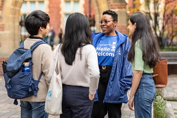 An International welcome team ambassador wearing a blue top talking to three students on campus