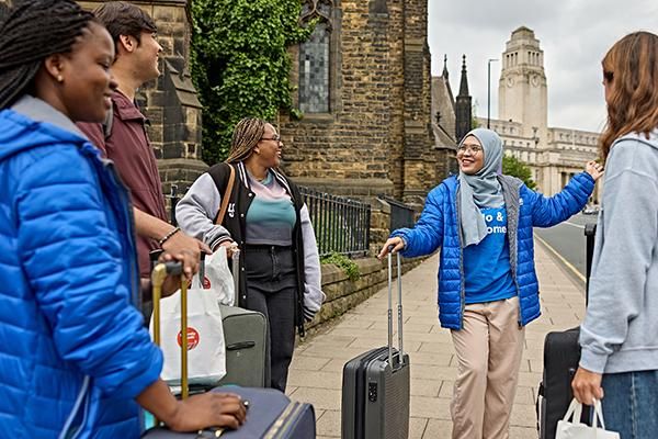 A Welcome team ambassador greeting students with suitcases in front of the Parkinson building