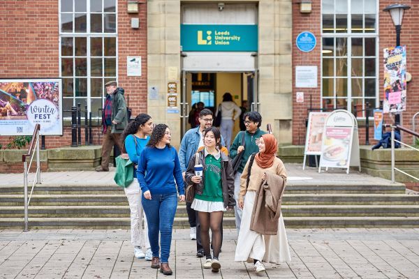 A group of students walk out of the entrance of Leeds University Union and towards the camera.