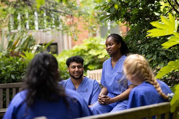 A group of medical students sitting outside in scrubs surrounded by greenery