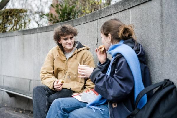 A student talking with an experienced peer while eating a sandwich.