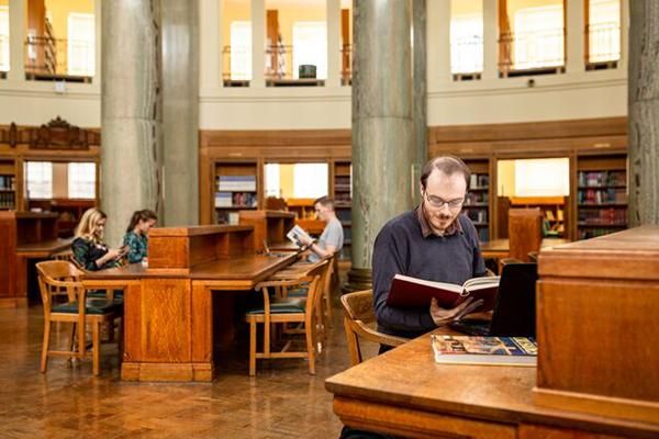 Postgraduate research student sitting at a desk in the Brotherton Library reading a book.