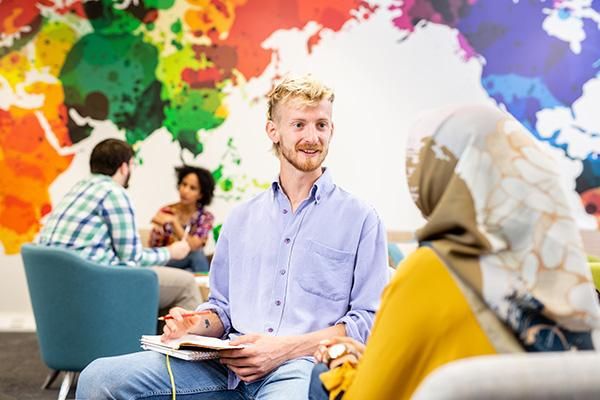 Postgraduate research students siting inside a large communal space with a world map on the wall.
