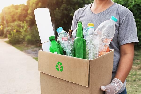 Arms holding a box that contains recyclable items like glass and plastic bottles