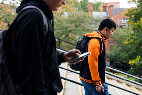 Two students walking down steps on campus. One is using a mobile phone.