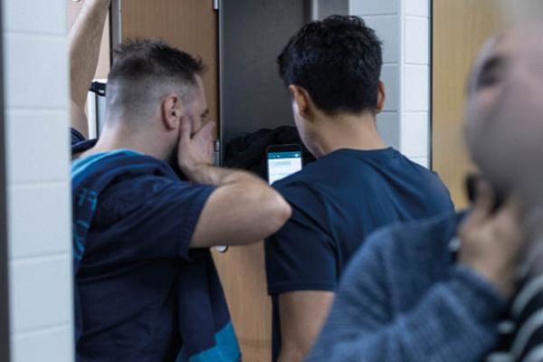 Two people in a locker room looking shocked at something on a phone screen