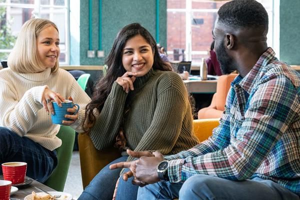 Three students sat in a bright comfy social space, drinking coffee and chatting